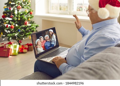 Online communication in quarantine and staying in touch with relatives. Grandfather in Santa hat sitting on sofa at home on Christmas Day, video calling family and waving hand happy to see grandkids - Powered by Shutterstock