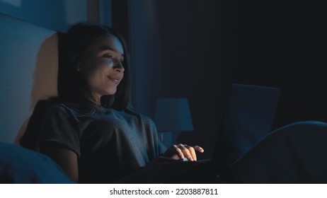 Online Connection. Sleepless Woman. Virtual Life. Pretty Smiling Lady In Bed Scrolling Laptop In Light Shadow Room Interior.