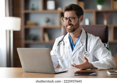 Online Consultation. Handsome Male Doctor Teleconferencing With Patient Via Laptop, Smiling Physician Man Sitting At Desk And Making Video Call On Computer, Enjoying Telemedicine, Copy Space - Powered by Shutterstock