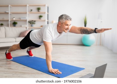 Online Domestic Sports. Senior Man Exercising To Video On Laptop Computer, Doing Plank And Raising One Arm, Working Out At Home On Mat, Keeping His Body Fit During Covid-19 Isolation