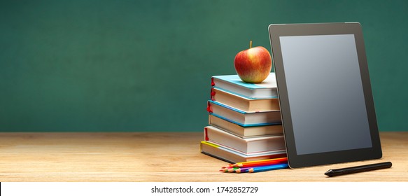 Online education. Books and tablet on the desktop on blackboard background. Copy space for text