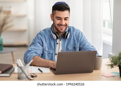 Online Education Concept. Portrait Of Happy Jewish Man In Kipa And Headset Working Or Studying Remotely At Home Office, Looking At Screen Typing On Keyboard, Using Laptop And Sitting At Desk