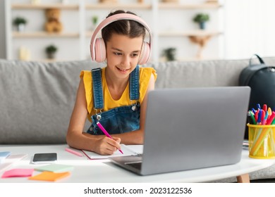 Online Education Concept. Smiling young teenage girl in headphones sitting at desk, using laptop writing or drawing in her paper notebook with colorful marker. Schoolgirl doing creative homework - Powered by Shutterstock