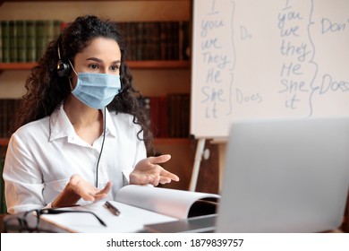 Online Education During Pandemic Concept. English Teacher Having Video Call With Students And Class Group, Using Laptop Computer. Woman Wearing Headphones And Medical Mask, Explaining Grammar Rules