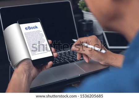 Online education, E-learning concept. Man reading ebook while working on laptop computer. Student reading Ebook via book e-reader application on mobile smart phone in library, close up
