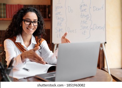 Online Education. Female English teacher having video conference chat with students and class group, using laptop. Woman wearing glasses and wireless earphones, talking to webcam, explaining