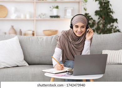 Online Education For Muslim Women. Happy Arabic Girl In Headscarf And Headset Studying With Laptop At Home, Taking Notes While Watching Webinar - Powered by Shutterstock