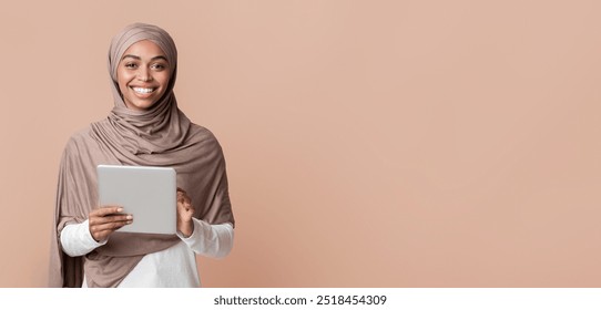 Online Education For Muslims. Portrait of happy afro muslim woman in hijab with digital tablet in hands over yellow background in studio, free space - Powered by Shutterstock