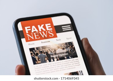 Online fake news on a mobile phone. Close up of woman reading Fake news HOAX or articles in a smartphone screen application. Hand holding smart device. Mockup website. Fake Newspaper portal.