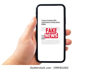 Online Fake News On A Mobile Phone. Man Holding A Smartphone With Fake News In Front Of The Monitor With Fake News. Propaganda, Misinformation And Hoax Concept.