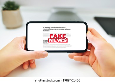 Online Fake News On A Mobile Phone. Woman Holding A Smartphone With Fake News In Front Of The Monitor With Fake News. Propaganda, Misinformation. Horizontal Photo.