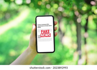 Online Fake News On A Mobile Phone. Holding A Smartphone With Fake News On Vineyard Background. Propaganda, Misinformation And Hoax Concept. 