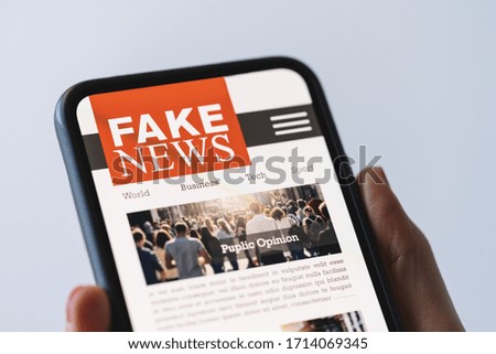 Online fake news on a mobile phone. Close up of woman reading Fake news HOAX or articles in a smartphone screen application. Hand holding smart device. Mockup website. Fake Newspaper portal.