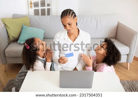 Online Family Shopping. Black Preteen Daughters Asking Mom With Credit Card And Laptop To Buy Something, Holding Hands In Prayer Gesture While Purchasing Things Together At Home