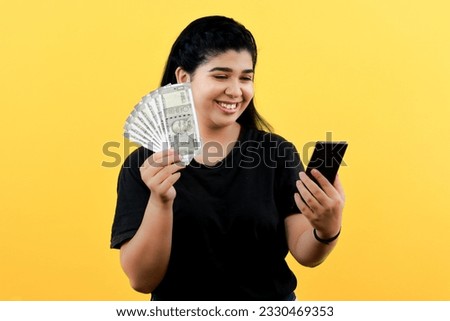 Online Fantasy Sports Money Winner Young Indian Female Posing with ₹500 Currency Notes and Smiling While Looking at Mobile Screen