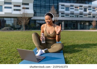 Online Fitness Class. Young African American Woman In Headphones Greeting Personal Coach On Laptop At City Park. Millennial Black Lady Talking To Trainer On Web, Drinking Water During Outdoor Training