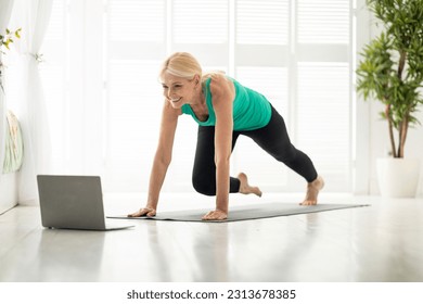 Online Fitness. Sporty mature lady doing exercises in front of laptop at home, active senior woman watching video tutorials and practicing sports, working out on yoga mat, training in living room - Powered by Shutterstock