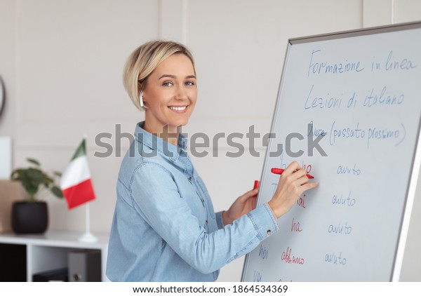 Online foreign languages school. Positive female\
teacher writing on blackboard, teaching Italian on web, explaining\
grammar rules to students. Happy young tutor giving lecture on\
internet