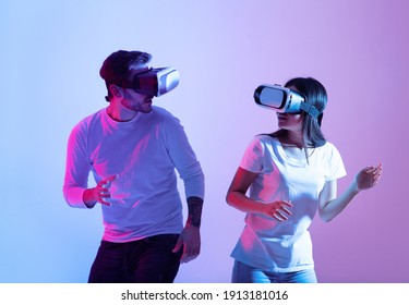 Online Game, Fun Together, Entertainment And Modern Active Date. Cheerful Young Guy And Asian Lady In Virtual Reality Glasses Look At Each Other And Play As Team, In Neon, Studio Shot, Free Space