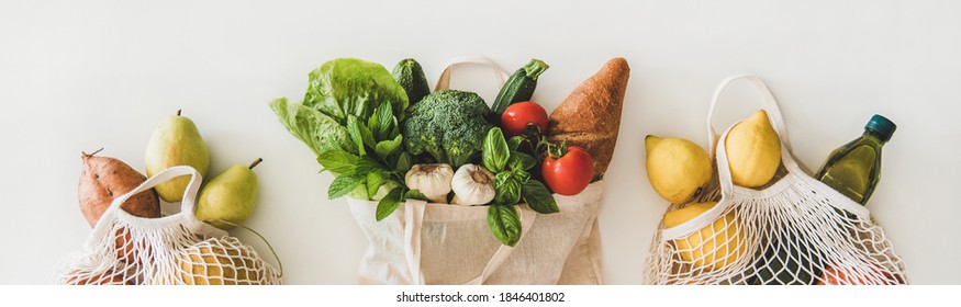 Online grocery healthy shopping. Flat-lay of fruit, vegetables, greens, bread and oil in eco-friendly bag over white background, top view, wide composition. Shop online during pandemic of coronavirus