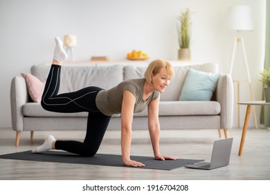 Online home fitness concept. Beautiful mature woman exercising to sports video on laptop in living room. Fit senior lady working out, keeping in good shape indoors during covid lockdown - Powered by Shutterstock
