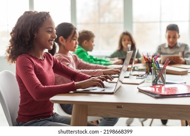 Online Learning. Black Schoolgirl Using Laptop Sitting At Desk With Multiethnic Classmates In Classroom Indoor. Modern School Education And Technology Concept. Selective Focus - Powered by Shutterstock