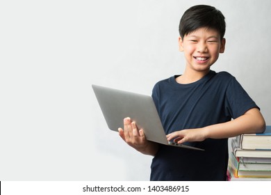 Online learning concept. A smart looking Asian boy standing with a computer laptop and a tall stack of colorful and various types of text books beside him. E-learning, Gamification, Self- Study.  - Powered by Shutterstock
