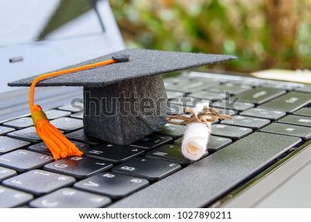 online learning or e-learning and online graduate certificate program concept : Black graduation cap, diploma on a laptop computer keyboard, depicts distant learning can be done via cyber / internet