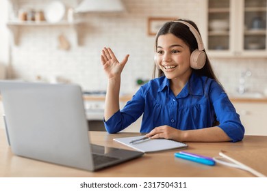 Online Learning Excellence. Schoolgirl With Headphones Raising Hand During Video Call Lesson, Learning Remotely Via Laptop Computer Sitting At Desk At Home. E-Learning Success Concept - Powered by Shutterstock