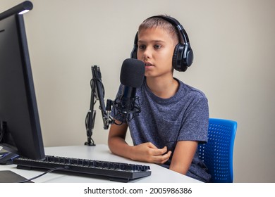 Online learning, remote education, gaming, school concept. Teenage boy wearing headphones using microphone playing video games online on computer, recording podcast, online learning from home - Powered by Shutterstock