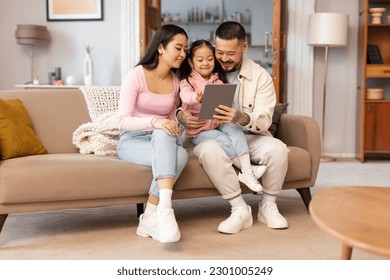 Online Leisure For Family. Happy Japanese Parents And Child Daughter Using Digital Tablet Browsing Internet And Watching Cartoons Online Sitting On Sofa At Home. Weekend Together Concept - Powered by Shutterstock