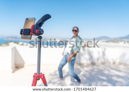 Online lessons of modern dance, young woman dancing in front of a smartphone on a tripod on the roof of a bright sunny day.