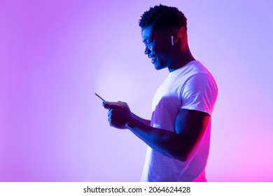 Online Life Concept. Millennial Black Guy Using Mobile Phone, Checking Web Or Social Media In Neon Light, Copy Space. Cool African American Man Holding Modern Gadget, Messaging On Internet