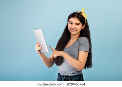 Online life. Smart Indian teen girl using tablet pc for remote studies on blue studio background. Intelligent Eastern adolescent having conference on touch pad, communicating on web
