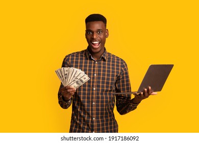 Online Lottery. Excited Black Guy With Dollar Cash And Laptop Celebrating Success, Overjoyed African American Man Holding Money And Computer, Standing Isolated Over Yellow Background, Free Space