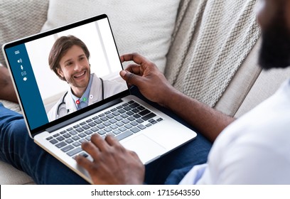 Online Medical Consultancy. Unrecognizable Black Man Having Video Call With His Doctor, Using Laptop At Home, Over Shoulder View