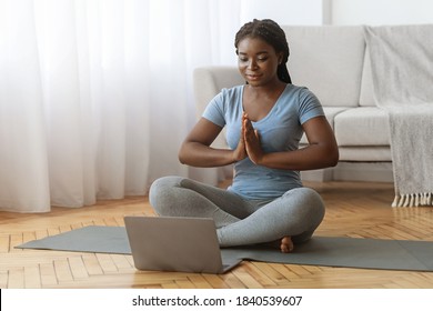 Online Meditation. Calm Black Lady Practicing Yoga In Front Of Laptop At Home, Meditating In Lotus Position, Sporty African American Woman Sitting With Clasped Hands On Mat In Living Room, Copy Space - Powered by Shutterstock