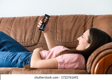 Online Meeting With Friends. A Young Woman Is Using Smartphone For Video Call, He Lays On Couch And Talks With A Friend In Cozy Homely Atmosphere. Apps For Video Communication, Zoom. Side View