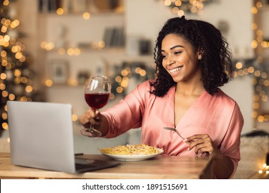 Online Meeting. Happy Beautiful Black Woman Making Video Call With Friends Or Husband During Dinner, Drinking Red Wine And Toasting, Sitting At Dining Table, Eating Pasta, Celebrating Alone At Home