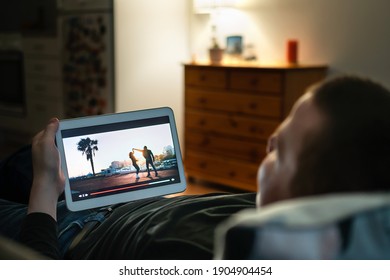 Online Movie Stream In Tablet Screen Home At Night. Man Watching On Demand Film Streaming Service Or Music Video. Tv Series In VOD Site Or App. Person Enjoying Entertainment On Cozy Couch In Dark.