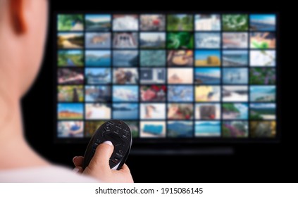 Online Multimedia video concept on TV set in dark room. Woman watching online TV with remote control in hand. Multimedia streaming VoD content provider concept.