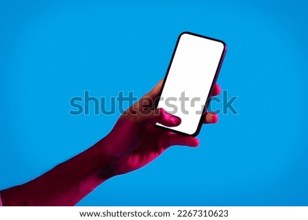 Online offer, mobile app. Cropped of african american man hand holding modern cell phone with white blank screen on blue studio background in neon light, mockup for advertisement, copy space