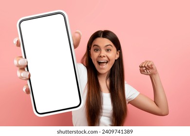 Online offer. Overjoyed teen girl celebrating success, shake fists and showing big phone with white blank screen at camera, emotionally reacting to win while standing over pink background, copy space - Powered by Shutterstock