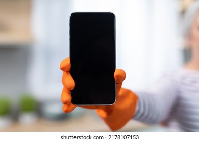 Online Offer. Unrecognizable Lady Wearing Rubber Glove Holding Big Blank Smartphone, Elderly Female Showing Mobile Phone With Black Screen At Camera, Recommending Cleaning Service App, Mockup