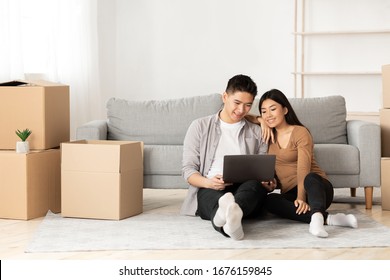 Online Ordering Concept. Asian family using laptop sitting on floor among boxes, empty space