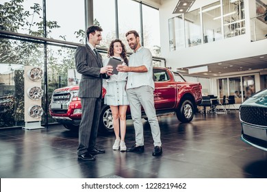 Online Payment. Beautiful Happy Couple Buying A Car At Car Salon Showroom Handsome Car Salesman Showing Something On A Digital Tablet To His Customers Lifestyle Communication Technology Online Device