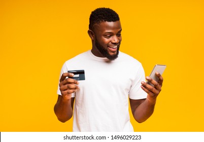 Online payment. Cheerful black man using credit card and smartphone for purchasing goods