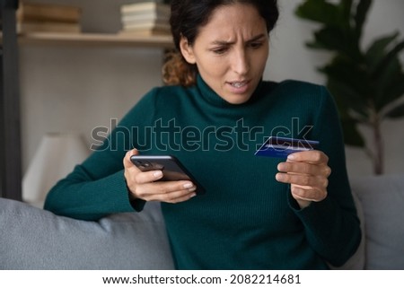 Online payment problem. Worried confused millennial latin female overspending too much money from credit card at web shopping via cell. Shocked frustrated young lady getting bank card declined blocked