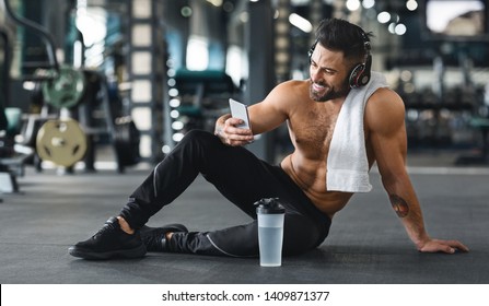 Online Personal Trainer On Mobile Phone. Muscular Man Using Cellphone At Gym, Free Space