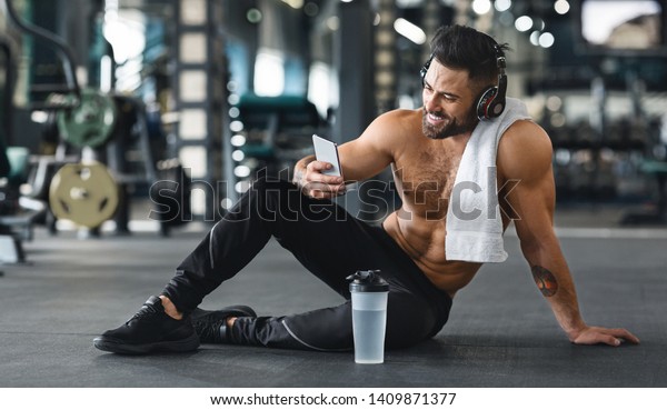 Online personal trainer on mobile phone.\
Muscular man using cellphone at gym, free\
space